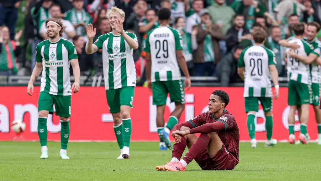Augsburg's Noahkai Banks sits disappointed on the floor while Bremen players celebrate