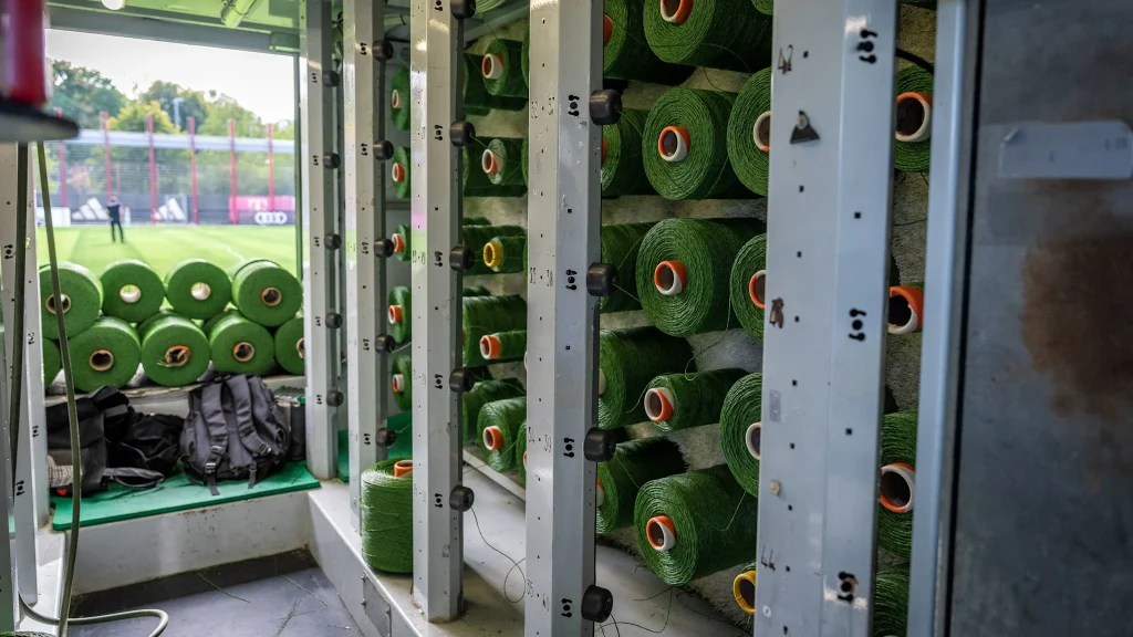 Rolls with kilometres of synthetic fibre, from which the blades of grass are cut and embedded, are stacked on several pallets.