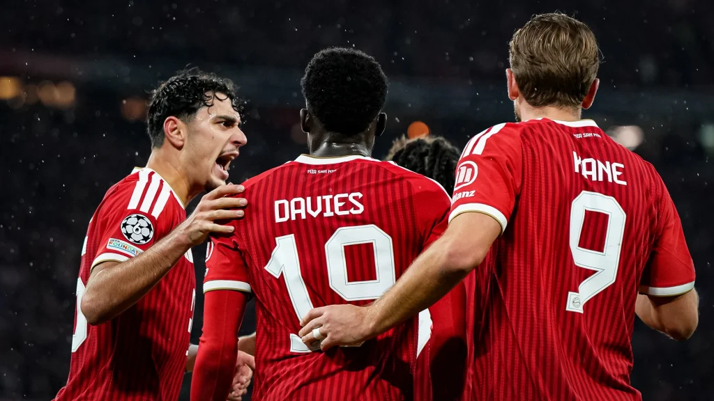 Aleksandar Pavlović, Alphonso Davies und Harry Kane jubeln Arm in Arm während des Champions League-Heimspiels des FC Bayern gegen den FC Arsenal