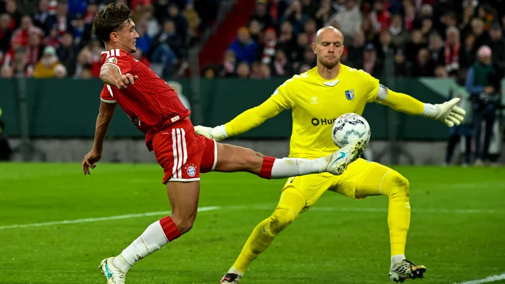 Tom Bischof versucht den Ball an Gäste-Keeper Reimann vorbeizuspitzeln im DFB-Pokalspiel des FC Bayern gegen den 1. FC Magdeburg